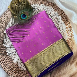 May include: A vibrant magenta fabric featuring a repeating pattern of small gold dots, finished with a wide, intricate gold metallic border and a deep blue edge. A single peacock feather and a decorative gold metal object are placed on top.