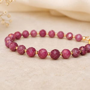 Peut inclure: Un bracelet de perles composé de pierres précieuses rondes et facettées d'un rose profond, alternées avec de petites perles d'espacement en métal doré poli. Le bracelet est doté d'un fermoir mousqueton en métal doré et d'un anneau.
