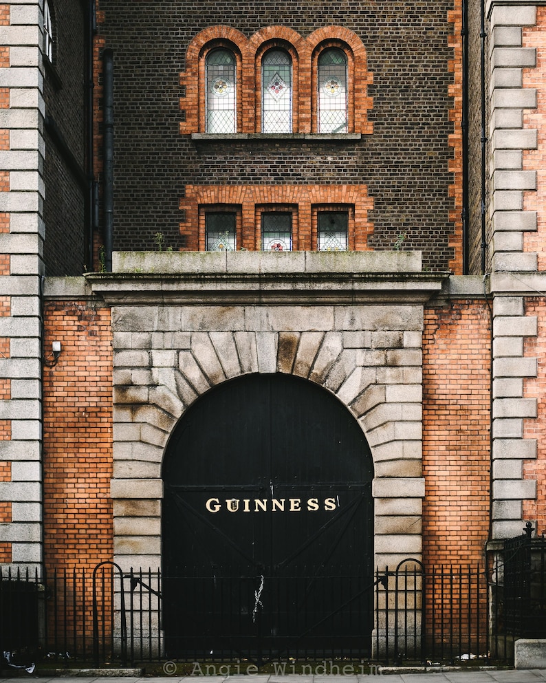 Puede incluir: Una puerta de metal negro con una entrada arqueada, ubicada en un edificio de ladrillo. La puerta tiene la palabra "GUINNESS" en letras doradas.