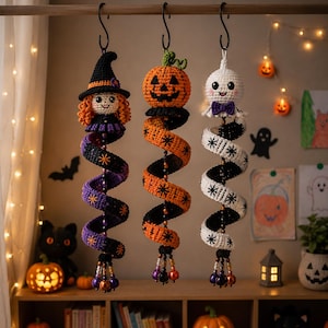 May include: Three hanging crochet decorations featuring a witch with a black hat, a jack-o'-lantern, and a white ghost. Each figure is attached to a long, spiraling tail patterned with stars, finished with dangling beads at the bottom ends.