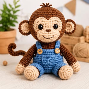 May include: A crocheted monkey toy with dark brown fur, a light beige face, and a curled tail. The monkey wears blue crocheted overalls featuring two small wooden buttons on the straps and a front pocket. It has black plastic safety eyes.