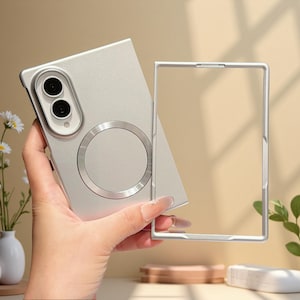 Può includere: Una custodia per smartphone color argento con finitura opaca, dotata di un anello magnetico circolare sul retro e di un modulo fotocamera rialzato con due lenti. La custodia include un telaio rettangolare argentato abbinato per lo schermo.