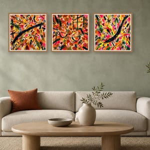Three framed square abstract art prints featuring vibrant brushwork hang above a beige sofa in a neutral living room setting.