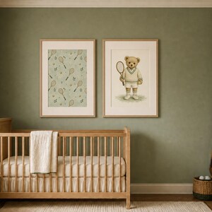 Two framed prints hang above a wooden crib against a sage green wall.