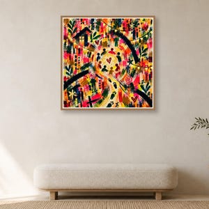A framed square abstract print centered on a plain wall above a long upholstered bench and side table with greenery.