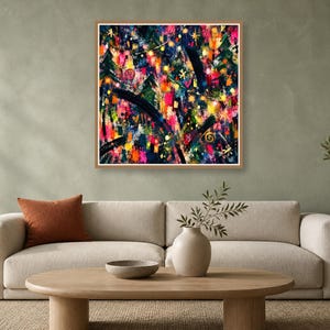 A square abstract artwork with a thin wooden frame hangs on a sage green wall above a cream-colored sofa and wooden coffee table.