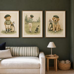 K&ouml;nnte beinhalten: Drei gerahmte Wandbilder mit Aquarellillustrationen eines Teddyb&auml;ren mit Golftasche, einer Person beim Golfschwung auf einem Platz und eines Golden Retriever Welpen mit gr&uuml;ner M&uuml;tze, alle in hellen Holzrahmen pr&auml;sentiert.