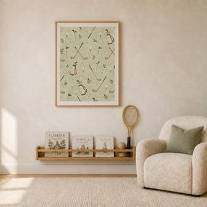 A framed golf print hangs above a wooden picture ledge and a cream-colored armchair in a cozy nursery room.