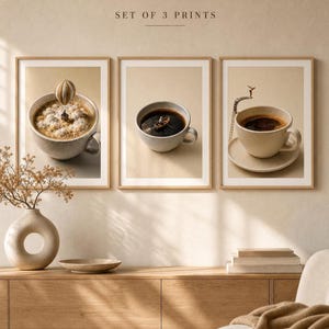 A mockup showing three framed art prints of coffee-themed miniature photography hanging above a wooden console table with a vase of dried stems and stacked books.