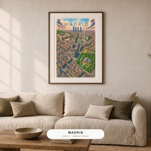 May include: A framed vertical art print featuring a detailed, colorful aerial illustration of the city of Madrid, Spain. The artwork displays dense urban architecture, green park spaces, and a skyline under a blue sky with the text MADRID.