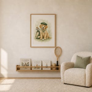 May include: A framed watercolor print of a golden retriever puppy wearing a green cap and a blue scarf, sitting next to a golf bag and ball. The artwork is displayed on a wall above a wooden shelf holding three books and a vintage tennis racket.
