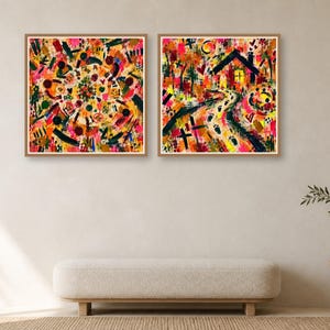 Two square framed abstract art prints hanging side by side on a neutral wall above a tufted bench and a wooden side table with a plant.