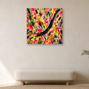 A square abstract art print featuring colorful gestural brushstrokes hangs centered on a plain wall above a low cream bench.
