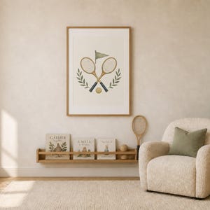 May include: A framed wall art print featuring a watercolor illustration of two crossed vintage tennis rackets, a small tennis ball, a green flag, and two laurel branches. The artwork is displayed in a light wood frame on a neutral wall.