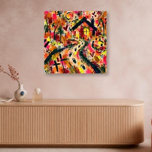 A square abstract print hangs unframed on a warm pinkish-gray wall above a long ribbed wooden credenza styled with a ceramic vase and perfume bottles.