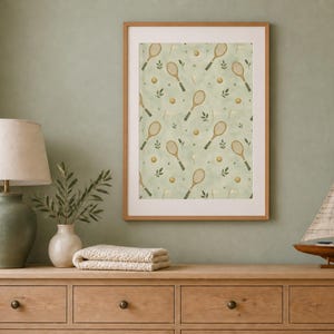 The framed tennis racket print sits above a wooden dresser next to a green lamp and model sailboat.