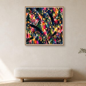 A framed square abstract print hangs on a plain cream wall above a long upholstered bench and a small side table with a vase.