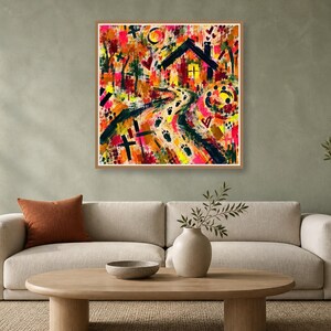A square abstract print in a wooden frame mounted on a gray wall above a beige couch, wooden coffee table, and side plant.