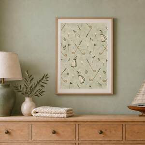 A framed golf wall art print sits on a wooden dresser beside a lamp, a vase, and a decorative model sailboat.