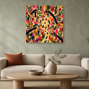 A square abstract artwork hanging on a green wall above a beige sofa with a round wooden coffee table and plant.