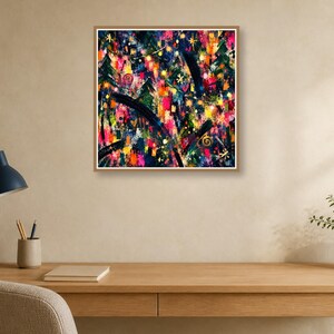 A framed square abstract art print hangs on a light tan wall above a wooden desk with a blue lamp, notebook, and pencils.