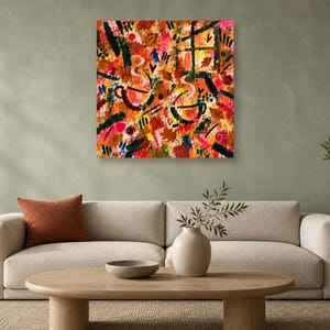 A square abstract art print featuring warm autumn colors hangs on a green wall above a beige sofa with a rust-colored pillow.