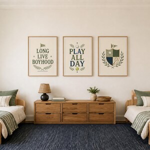 May include: Three framed wall art prints featuring sports-themed illustrations and text. The left print reads LONG LIVE BOYHOOD, the center print reads PLAY ALL DAY, and the right print features a shield crest with a golf ball and tennis racket.