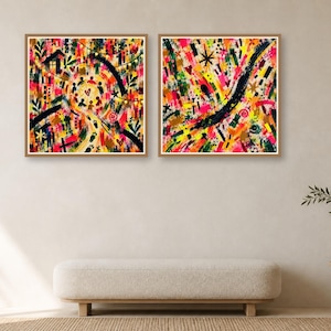 Two square wood-framed abstract art prints hang side by side above a low cream bench against a neutral wall.