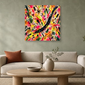 A square abstract art print with vivid pink, yellow, green, and black brushstrokes hangs above a beige sofa on a pale green wall.
