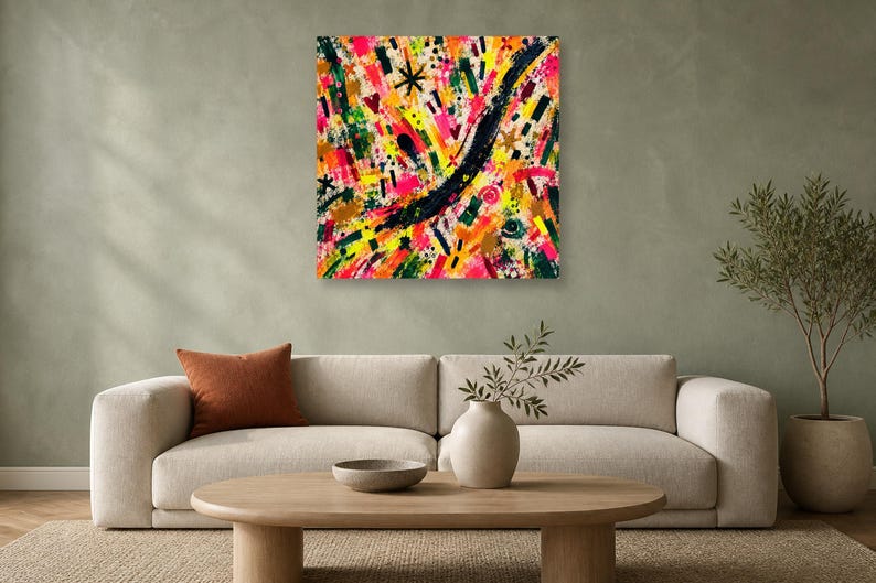 A square abstract art print with vivid pink, yellow, green, and black brushstrokes hangs above a beige sofa on a pale green wall.