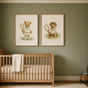 May include: Two framed wall art prints featuring a teddy bear and a golden retriever puppy, both dressed in white tennis attire and holding tennis rackets. The prints are displayed in light wood frames on a sage green wall above a wooden crib.