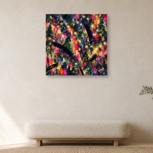 A single square colorful abstract art print hangs on a plain cream-colored wall above a long beige bench and a small wooden side table with a plant.