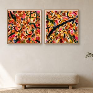 Two framed square abstract art prints with warm colored brush strokes hang on a plain wall above a long low bench.
