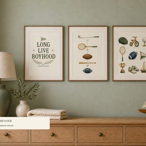 May include: Three framed wall art prints featuring vintage-style illustrations of sports equipment and the text "LONG LIVE BOYHOOD". The prints are displayed in thin wooden frames, showcasing items like a tennis racket, football, baseball bat, and a trophy.