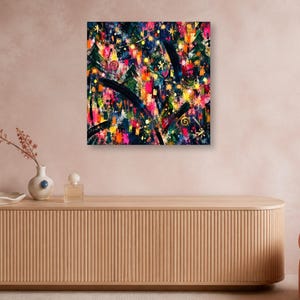 A square abstract artwork hangs on a pinkish wall above a long wooden credenza featuring a small vase, perfume bottle, and dish.