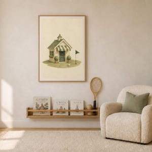 May include: A framed wall art print featuring a light-colored cottage with a green roof and striped awning, situated on a small patch of grass with a golf flag and ball. The illustration is rendered in soft, muted tones on a cream-colored background.
