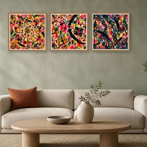 A staged living room with a beige sofa, a wooden coffee table, a potted plant, and three square abstract paintings hung on a green wall.