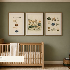 May include: Three framed wall art prints featuring illustrations of sports equipment and a group of anthropomorphic animals in athletic attire. The prints are displayed in light wood frames above a wooden crib in a room with sage green walls.