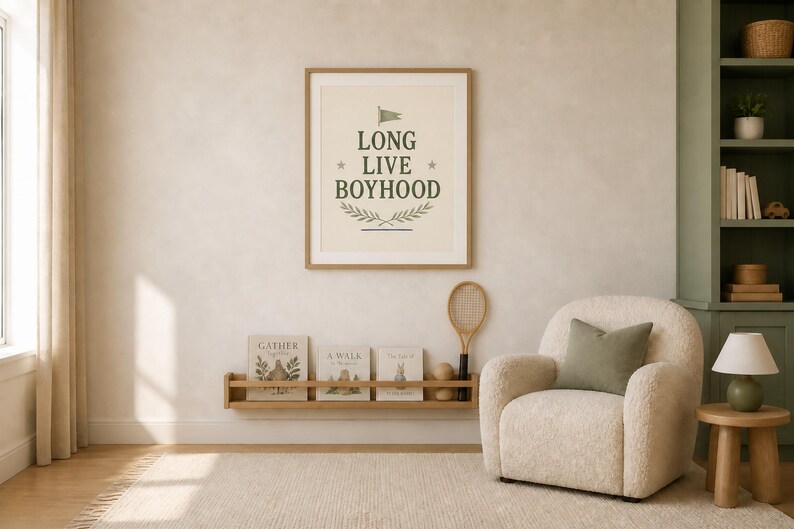 Puede incluir: Un cuadro de pared con el texto LONG LIVE BOYHOOD en letras de color verde oscuro, acentuado por una peque&ntilde;a bandera, dos estrellas y un dise&ntilde;o de rama de laurel. El cuadro se muestra sobre un estante de madera con tres libros y una raqueta.