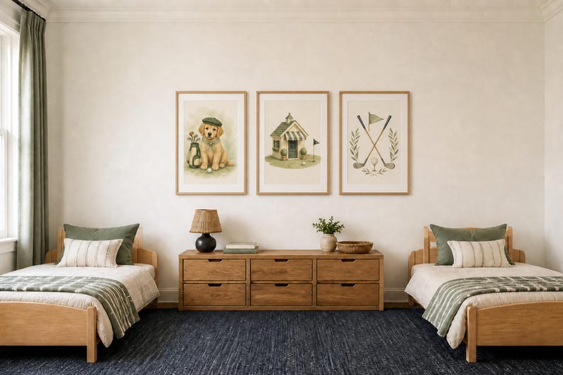 May include: Three framed wall art prints featuring golf-themed illustrations: a golden retriever puppy wearing a cap, a small clubhouse building, and crossed golf clubs with a flag. The prints are displayed in light wood frames on a white wall.