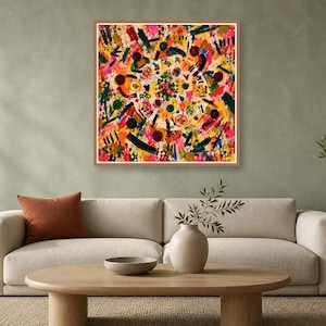 A square framed abstract painting with rich colors hangs on a sage green wall above a beige sofa and wooden coffee table.