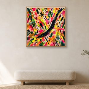 A square wood-framed abstract art print hangs centered above a low cream bench against a neutral wall with a side table.