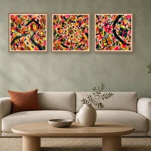 Three square framed abstract art prints featuring colorful textured patterns displayed on a pale green wall above a neutral sofa.
