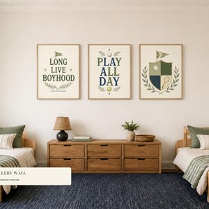 May include: Three framed wall art prints featuring sports-themed illustrations and text. The left print reads LONG LIVE BOYHOOD, the center print reads PLAY ALL DAY, and the right print features a shield crest with a golf ball and tennis racket.