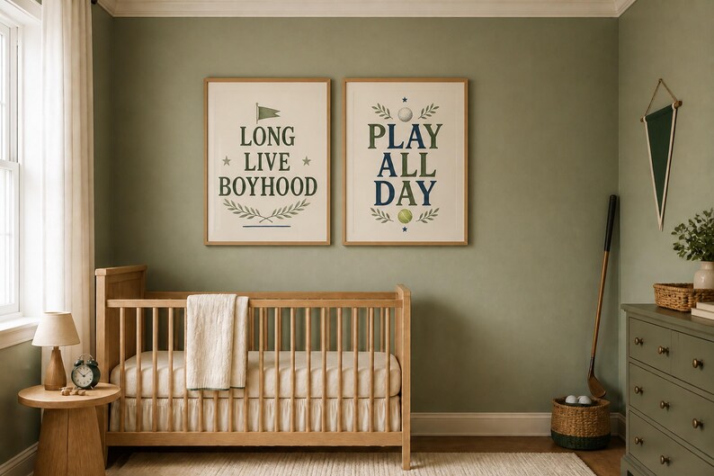 Puede incluir: Dos l&aacute;minas decorativas enmarcadas con bordes claros colgadas sobre una cuna de madera. La l&aacute;mina de la izquierda presenta el texto LONG LIVE BOYHOOD con una bandera y motivos de hojas. La de la derecha muestra PLAY ALL DAY con una pelota de golf.