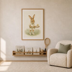 May include: A framed wall art print featuring a brown rabbit dressed in white tennis attire, holding a wooden tennis racket and a yellow ball. The illustration is set against a soft cream background, depicting the rabbit standing on a tennis court.