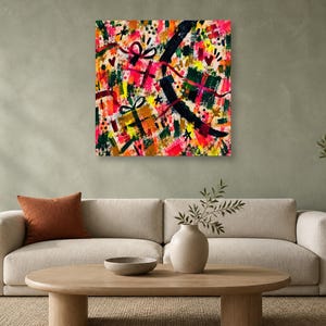 A square colorful abstract art print hangs on a light green wall above a beige sofa with an orange pillow.