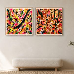 Two square wood-framed abstract art prints hang side by side on a neutral wall above a long low bench.