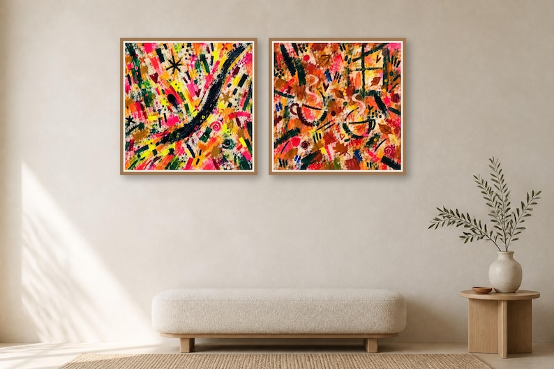 Two square wood-framed abstract art prints hang side by side on a neutral wall above a long low bench.