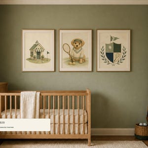 May include: Three framed wall art prints displayed above a wooden crib. The prints feature a golf clubhouse, a golden retriever puppy wearing a tennis outfit and holding a racket, and a crest with a golf ball, club, and laurel leaf design.